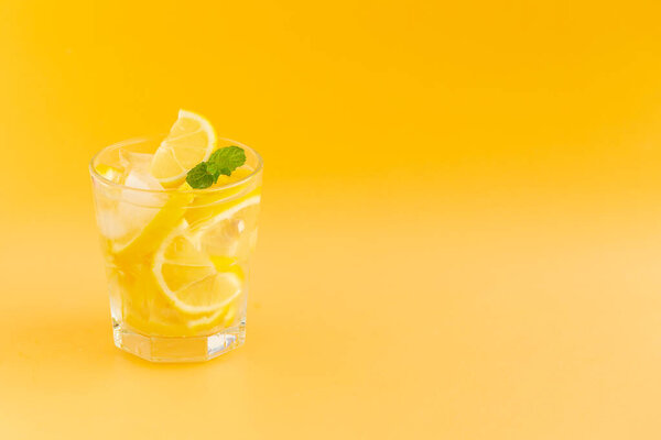 Детоксикация воды с лимоном в стакане на оранжевом фоне.