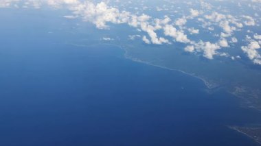 Nefes kesen bir hava görüntüsü derin mavi okyanusu ve sürüklenen bulutların altındaki karayı gözler önüne seriyor..
