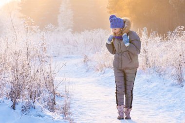 Güzel bir kadın kış ormanında karlı ağaçların arasında duruyor ve ilk karın tadını çıkarıyor.