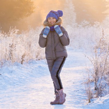 Güzel bir kadın kış ormanında karlı ağaçların arasında duruyor ve ilk karın tadını çıkarıyor.