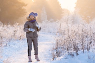 Güzel bir kadın kış ormanında karlı ağaçların arasında duruyor ve ilk karın tadını çıkarıyor.
