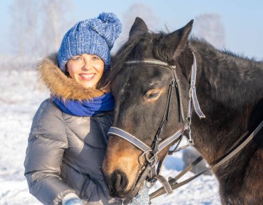 Güzel bir kadın kış ormanında karlı ağaçların arasında duruyor atıyla.