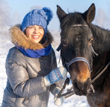 Güzel bir kadın kış ormanında karlı ağaçların arasında duruyor atıyla.
