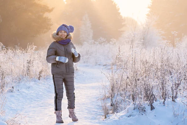 Güzel bir kadın kış ormanında karlı ağaçların arasında duruyor ve ilk karın tadını çıkarıyor.