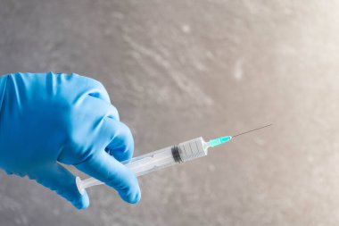 Doktorlar ellerinde ilaç şişesi ve gri arka planda temiz sıvı tutarken mavi lastik eldiven veriyorlar. Sıvı ilaç 2019-nCoV