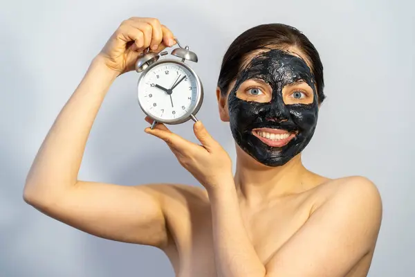 Känslomässig Kvinna Med Svart Träkol Ansikte Mask Och Väckarklocka Händerna — Stockfoto