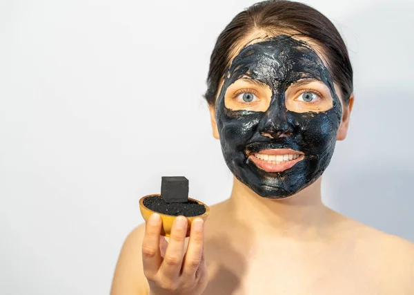 Emotional Woman with black charcoal face mask and friable coals in her hands.