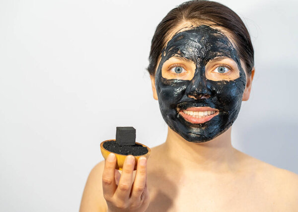 Emotional Woman with black charcoal face mask and friable coals in her hands.