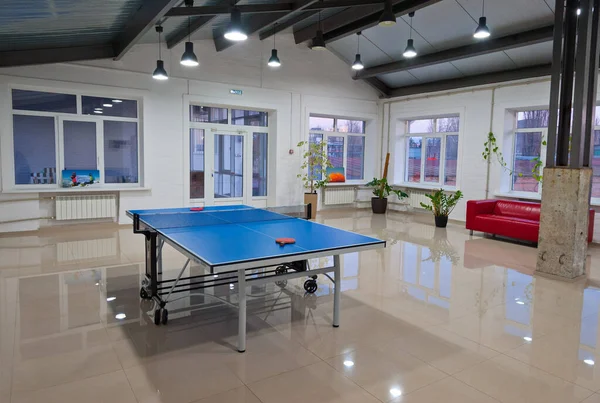 A room with a tennis table and shiny floor.