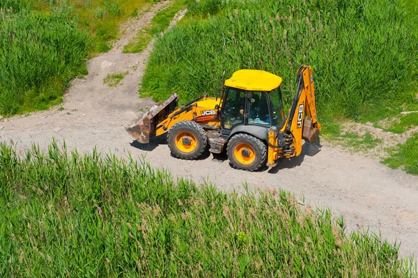 Tekerlekli kazıcı buldozer JCB 4CX toprak yolda ilerliyor. 