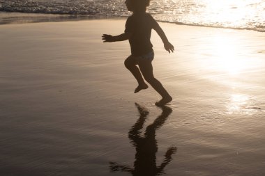 Mutlu çocuk plajda koşar. Güzel bir gün batımında suda genç bir çocuk silueti.