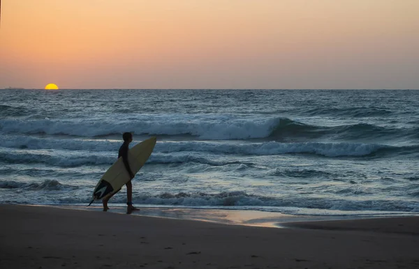 ビーチを歩く足のロープを持つ若いサーファー 地中海の美しい夕日と大きな波 サーファーの楽園 — ストック写真