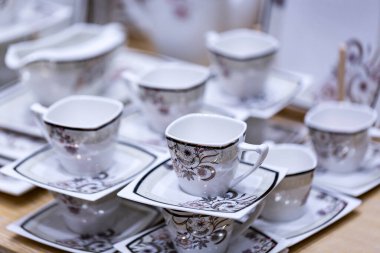 Tabaklar ve bardaklar beyaz tonda hafif ahşap bir masada duruyor. Seramik tabaklar, bardaklar, kupalar. Basit tasarım, yakın çekim üst görünüm. Mesajın için yer aç. Boş çay fincanları ve çay tabakları.