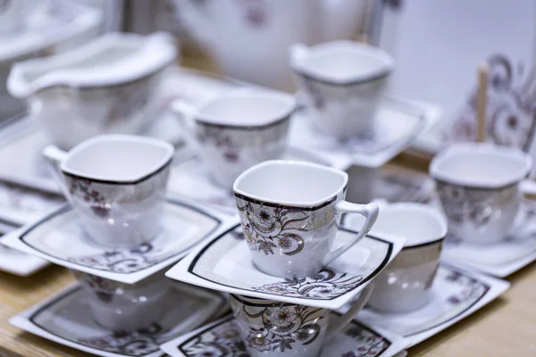 Tabaklar ve bardaklar beyaz tonda hafif ahşap bir masada duruyor. Seramik tabaklar, bardaklar, kupalar. Basit tasarım, yakın çekim üst görünüm. Mesajın için yer aç. Boş çay fincanları ve çay tabakları.