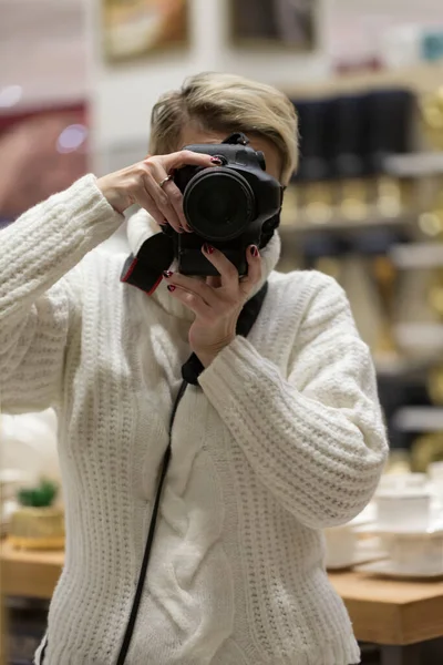 Woman with camera in hand stands in front of the mirror, takes a selfie. female photographer with camera taking picture of reflection. Reflection Of Woman Photographing In Mirror. Selective focus