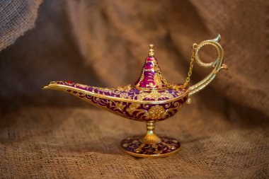 Çuval bezi kaplamalı altın sihirli lamba, yaklaş. Aladdin 'in Cin' le olan hikayesinden kalma arzuların lambası. Dilek, şans ve sihir kavramı. Seçici odaklanma. Herhangi bir tasarım için alanı kopyala