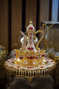 Doğu sürahisi bir tepside duruyor ve keten arka planda bakır bardaklar, yakın çekim. Doğu sofra takımı. Altın çaydanlıkta servis edilen Arap çayı. Süslü Arap sürahileri ve gözlük seçici odak noktası