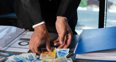İşadamı 'nın Elleri' nin elinde İsrail 'in Yeni Şekelleri' nin para yelpazesi var. Masaya para yığını saçılmış (Amerikan doları, nis banknotlar). El 'in kesilmiş görüntüsü banknotları tutuyor. Seçici odak
