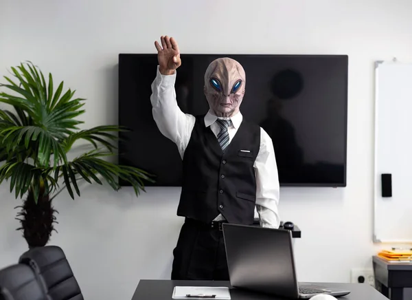 A humanoid Alien in a white shirt and business black suit in a conference, meeting room or home office raise your hand up. CEO martian putting his hand on his heart, standing, looking at camera