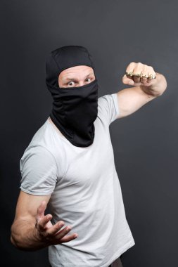 Pirinç muşta ile bir saldırı. Siyah maskeli sakallı bir adamın elinde metal muşta. Savaşta yasak silahlar, suçlu. Pirinç muştalı yumruğunu gösteren Amerikalı bir adam..
