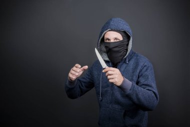 American hooded man with black mask holding knife and hand reaching, grabbing or attacking. Robbery, violence and economic crisis concept. Caucasian maniac, thief, gangster, rapist attack with knife. act of violence