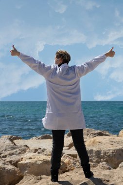 Mutlu özgürlük. Sarışın kadın. Kollarını açıp açık deniz ufkuna umutla bakıyor. Kaygısız Rus Kafkas Amerikalı doktor tıbbi maske ve beyaz önlüklü kameraya doğru.
