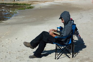 Gün batımında kumsalda kitap okuyan Amerikalı bir adam. Deniz manzaralı koltukta sigara içen Rus adam. Güneş gözlüğü, şapka ve kapüşonlu ceket giyen yakışıklı beyaz sakallı adam.