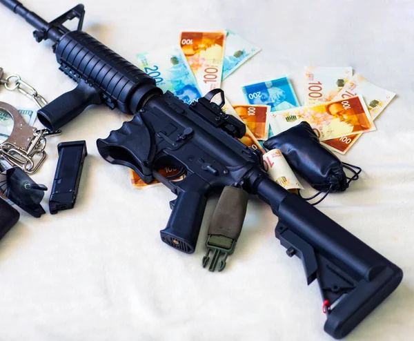 Modern automatic rifle, Pistol, gun and bullets 9mm ammunition, handcuffs on Israeli New Shekels and American dollars banknotes. Criminal money and punishment, Copy space. Financial Crime Banner