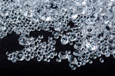 Elmaslar siyah arkaplanda. Mavi ve beyaz parlak mücevherler, metin için fotokopi alanı ile yan görünüm. Stüdyo çekimi, seçici odaklanma. Sahte Elmaslar Yığını. Plastik tanecikler. Kristallerin dağılması