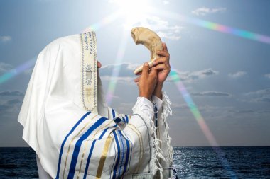 Tallit 'teki Yahudi haham gün batımında Rosh Hashanah' ın Shofar 'ını üflüyor. Trompet bayramı için shofar üfleyen Yahudi geleneksel tallith dua şalında koç boynuzunu üfleyen