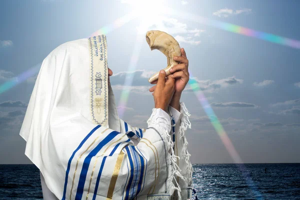 Tallit 'teki Yahudi haham gün batımında Rosh Hashanah' ın Shofar 'ını üflüyor. Trompet bayramı için shofar üfleyen Yahudi geleneksel tallith dua şalında koç boynuzunu üfleyen