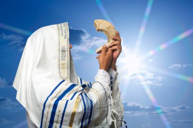 Tallit 'teki Yahudi haham gün batımında Rosh Hashanah' ın Shofar 'ını üflüyor. Trompet bayramı için shofar üfleyen Yahudi geleneksel tallith dua şalında koç boynuzunu üfleyen