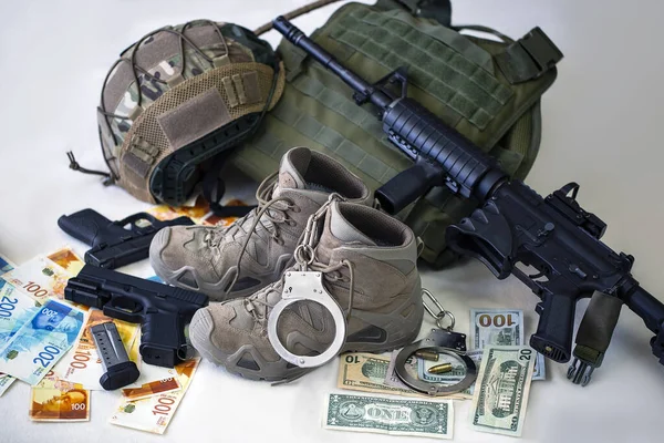 Military uniform and equipment, ammunition. Body armor, gun, bulletproof helmet, Modern automatic high powered rifle and military boots with banknotes of Israeli New Shekels, American dollar banknotes