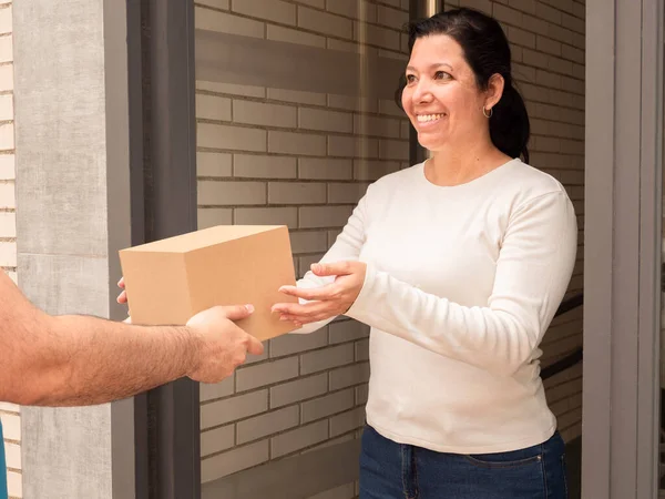 Caucasian woman receiving a box-shaped package without labels from a deliveryman or postman at her front door on the street