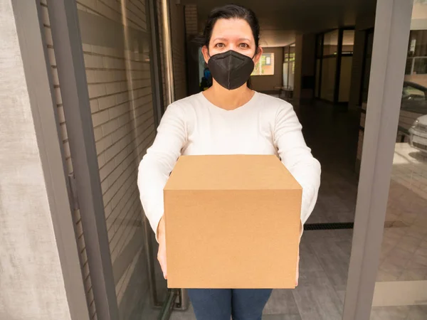 Beyaz bir kadın, kapıdaki postacıdan ya da teslimatçıdan etiketsiz bir paket alıyor.
