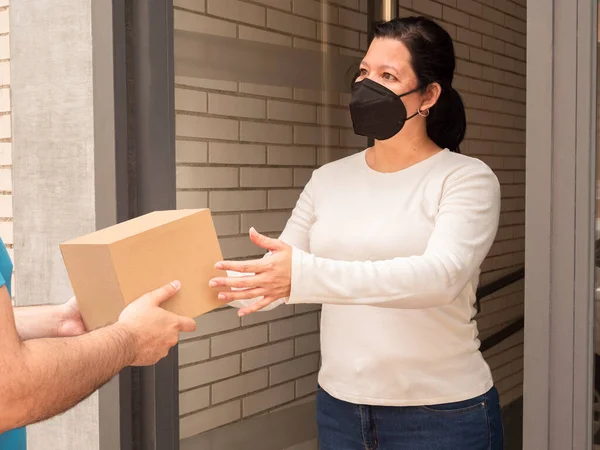 Caucasian woman receiving a box-shaped package without labels from a deliveryman or postman at her front door on the street