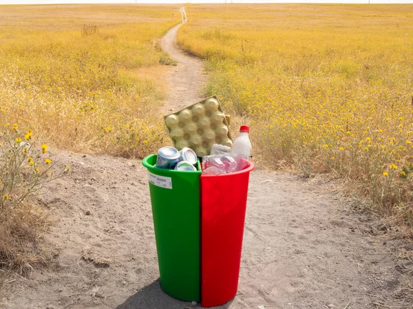 Üç geri dönüşüm kutusu, biri sarı, diğeri yeşil ve sonuncusu da siyah renkli plastik ve alüminyum geri dönüşümlü sarı renkli bir orman ve bir gün mavi gökyüzü.