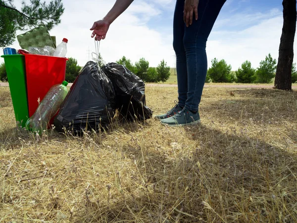 Ormandaki kadın geri dönüşüm atıklarını plastik karton ve alüminyumla geri dönüşüm kutularının yanına koyuyor. Kırmızı yeşil ve siyah teneke kutular.
