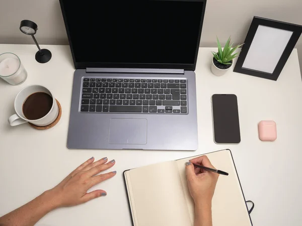 女人的手放在白桌子上 笔记本电脑在手机旁边的键盘上打字 黑色笔记本 白色蜡烛 小灌木丛和空白相框 — 图库照片
