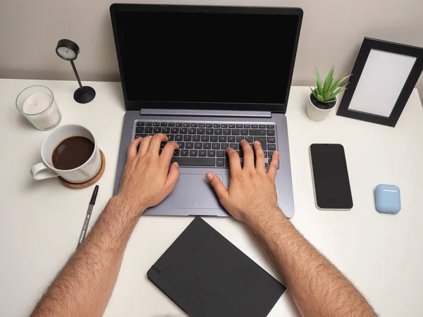男人的手放在白桌子上 笔记本电脑在键盘上打字 手机旁边 黑色笔记本 白色蜡烛 小灌木丛和空白相框 — 图库照片