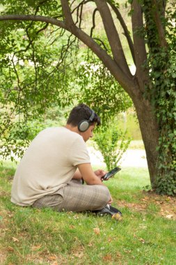 Latin esmer çocuk yeşil bir ormanda kulaklık ve sarı giysilerle müzik dinliyor.