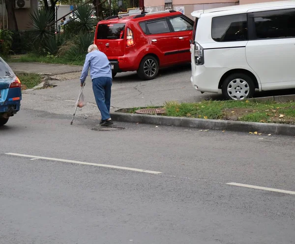 Koltuk değnekli yaşlı bir adam yolda yürüyor.