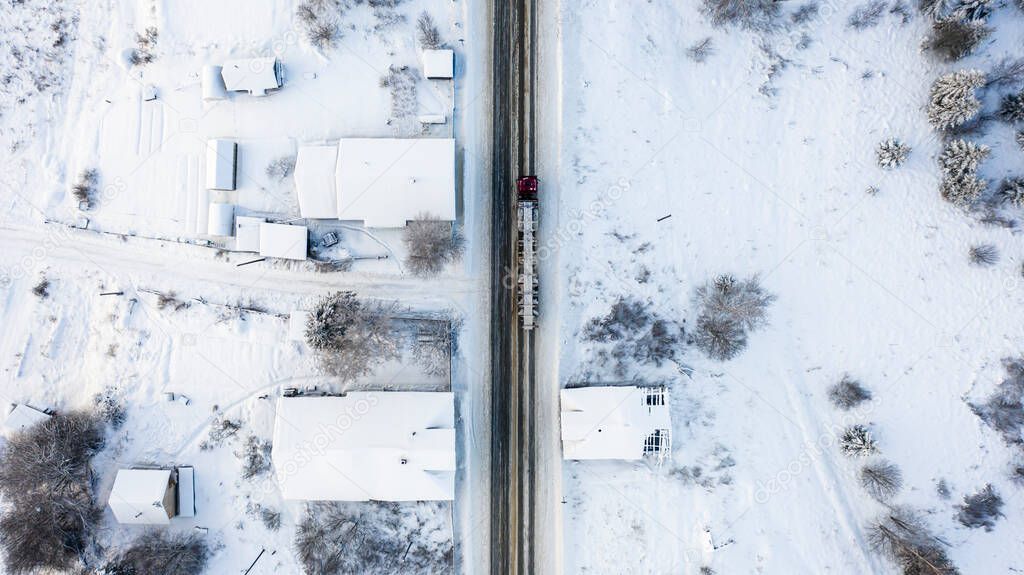  lorry timber truck driving loaded in winter forest on the highway through a snow-covered village, aerial photography