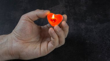 Koyu bir arka planda kalp şeklinde yanan bir mum bir adamın elinde