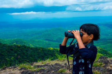 Hintli çocuk, dürbünle dağlara bakıyor, doğayı keşfediyor ve manzaranın tadını çıkarıyor. Merak, seyahat, macera ve açık hava öğrenimi kavramı.