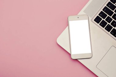 Modern pembe ofis masası ile beyaz ekranlı beyaz cep telefonunun fotokopi görüntüsü. Metni kopyalamak için dizüstü bilgisayarı var. Üst görünüm, düz yatış.