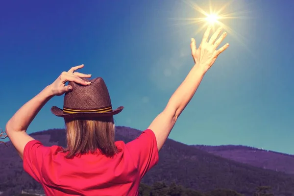 Back view of a woman in a clear windy day,  wearing a hat, gesture of touching the sun