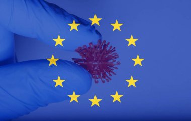 Avrupa 'da Corona Virüsü kavramının arka planında Avrupa bayrağı bulunan bir virüs hücresini tutan bir doktorun eli.