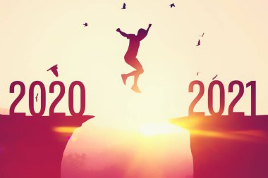 2020 'den 2021' e tropikal günbatımı plajında uçurumun arasında siluet adam zıplıyor. Özgürlük mücadelesi ve seyahat macera tatili konsepti. Klasik ton filtre efekti renk biçimi.