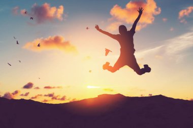 Siluet adam zıplıyor ve kuşlar gün batımında gökyüzünde uçuyor ve soyut arkaplan dokusunu bulutlandırıyor. İyi hissetme özgürlüğü ve seyahat macerası konseptini kopyala. Klasik ton filtre efekti renk biçimi.